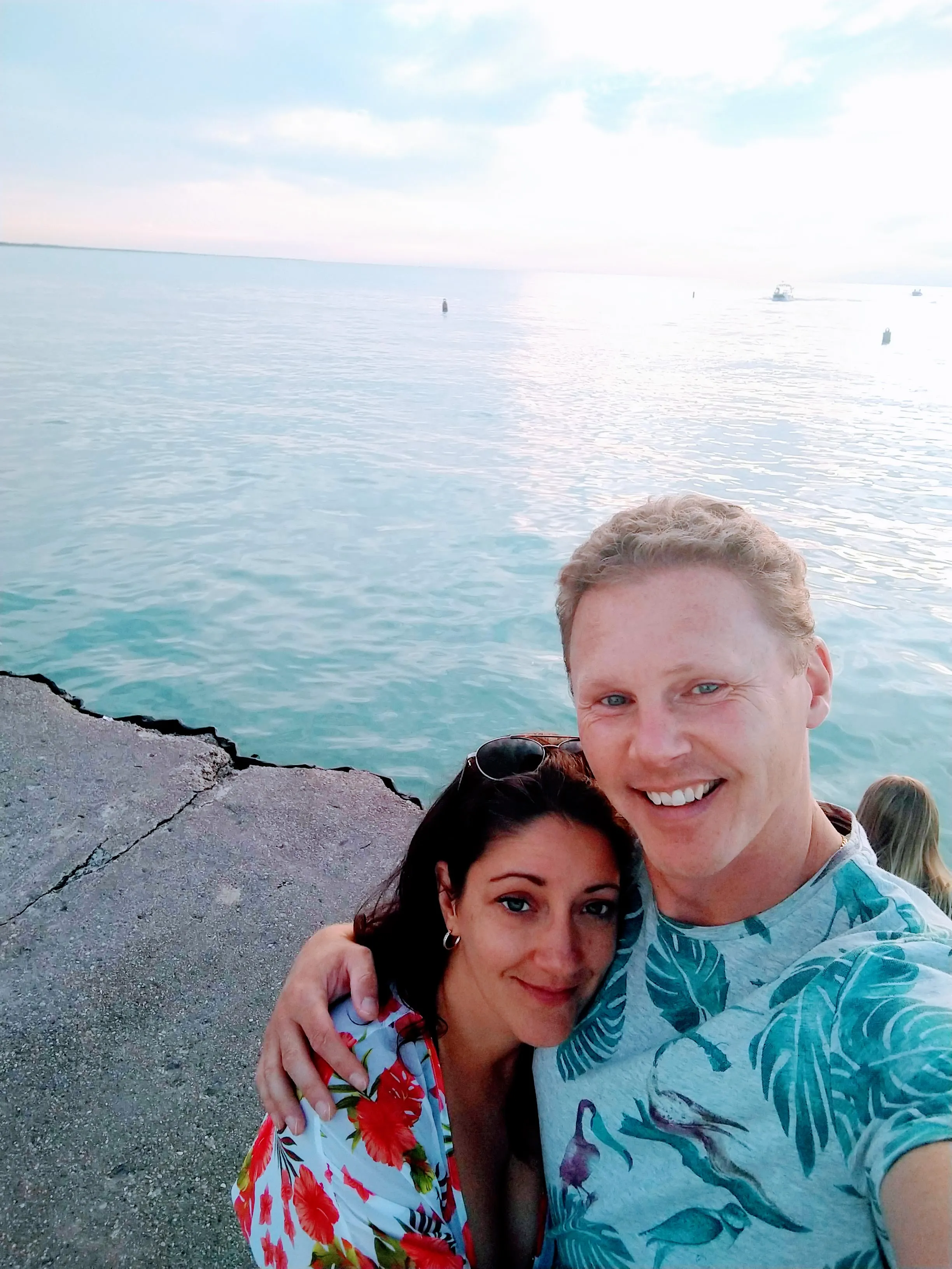 Chad and Liz on a seawall with turquoise water behind them.