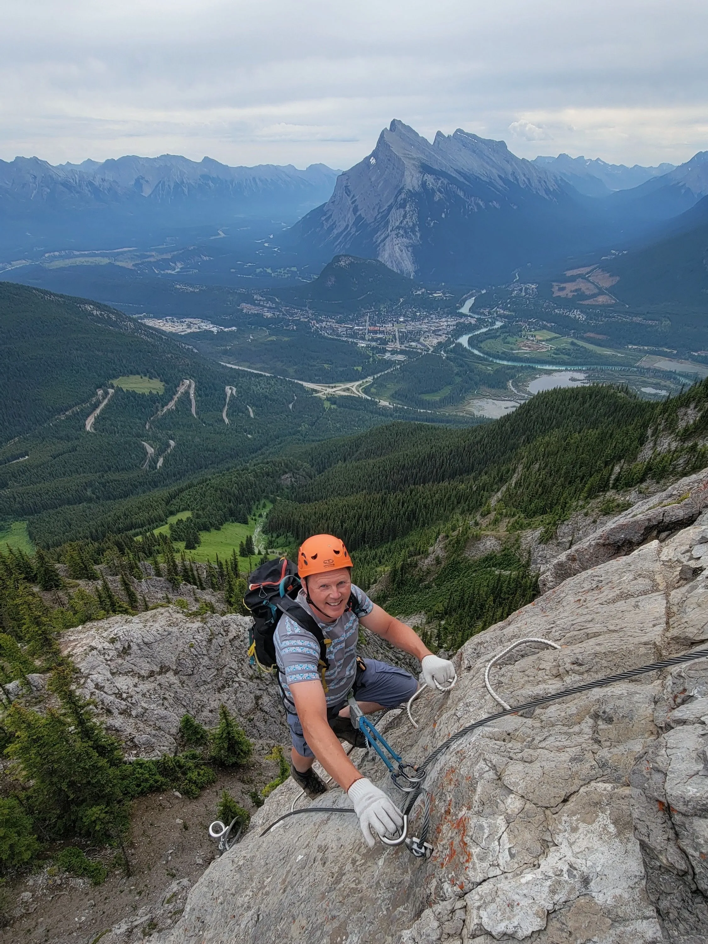 Chad on a via ferrata cable high above the valley, grinning back at the camera.